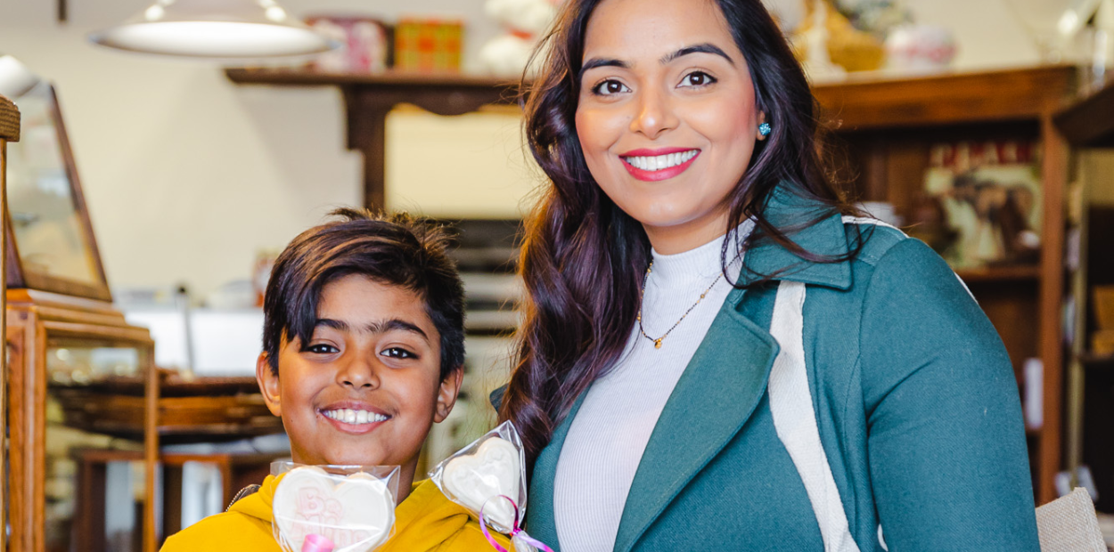 Mother and child in a chocolate shop holding heart-shaped lollipops.